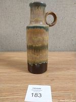 Front view of tall pottery jug showing color and shape with handle at the side.