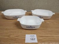 Photo showing the front view of the three CorningWare casserole dishes in white with blue cornflower pattern, no lids, displayed on a carpeted surface.