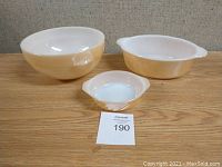 Front view of three Fire King bowls of different sizes showing the peach and cream exterior swirl pattern and white interiors.