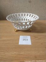 Side view of the white ceramic bowl showing open lattice sides, gold-accented rim, and three gold feet.