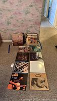 Stack of vinyl record albums lined up against wall, some laid out on carpet showing album covers including Jim Croce Greatest Hits, an album with a man wearing sunglasses, and others.
