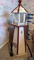Full view of tall wooden lighthouse tower with small glass wick diffuser at base, showing white panels with red trim and anchor decoration.