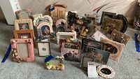 Lot of 23 small picture frames of varying sizes and styles, some with photos, arranged on carpeted floor