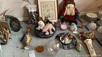 Table display showing collection of figurines, stuffed animals, decorative glassware, framed art and other home decor items in assorted styles and materials.