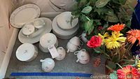 Full set of china dinnerware including plates, cups, creamer, sugar, and serving dishes with faux flowers grouped