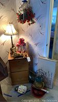 Photo showing the filing cabinet, tall lamp with cream shade, metal birdcage wall hanging with red flowers inside, and miscellaneous items including a white skull-shaped object and a couple of decorative pieces on top of the cabinet.