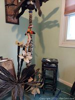 Full view of tall cloth palm tree with snake and toucan, standing next to two black lacquer nesting tables with floral design.