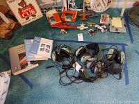 Four olive-green aviation headsets and softbound manuals laid out on carpet