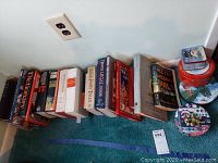 Photo showing a row of books stacked on carpet against wall, along with 4 decorative tins of varying sizes and Christmas or winter themes.