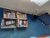 Photo showing four cardboard boxes containing mixed VCR tapes with various movie titles visible, placed on blue carpet