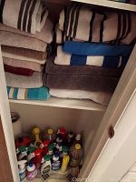 Photo showing folded bath towels in assorted colors and patterns on two shelves with cleaning supplies stored beneath.