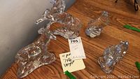 Four clear crystal animal figurines positioned on a wooden surface: horse, bird, moose, and bear figures.