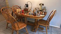 Full view of oak dining table with various decorations on top and four chairs around.