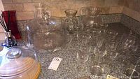 Glass cake plates with dome covers, assorted glassware glasses and plastic pitcher on kitchen counter.