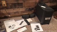 Main photo showing Bose CineMate subwoofer, two satellite speakers, remote control, and several manuals on carpeted floor next to wooden wall.