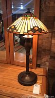 Full view of Tiffany style lamp on wooden surface, showing stained glass shade and metal base with on/off switch.