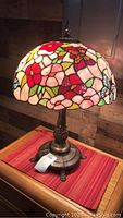 Side view of Tiffany style stained glass lamp with colorful floral and butterfly shade and bronze-colored base on wooden surface.