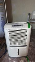 Frigidaire white dehumidifier unit showing front perforated vent and water level window with some dust visible on the surface