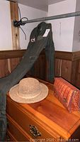 Flight suit hanging from rod above dresser with woven straw toucan hat and orange alligator purse on dresser.
