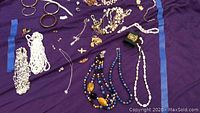 Overview of jewelry on purple cloth including necklaces, bracelets, earrings mostly diamonique and lapis beaded necklaces