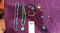 Full view of seven pieces of turquoise and silver jewelry including necklaces, earrings, and bracelet placed on purple fabric.