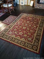 Larger and smaller red floral rugs shown side by side on dark wood floor with chair nearby