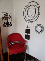 Photo of the upholstered Thomasville side chair with red fabric and wooden legs alongside three pieces of metal wall art and a round Westclox battery operated clock mounted on the wall.