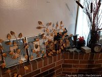 View of metal leaf and branch wall art above framed cat pictures on mantle, with other decorative items and vases to the right.