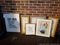 Three framed artworks leaned against a brick wall, showing various floral prints and one stated ready-made frame.