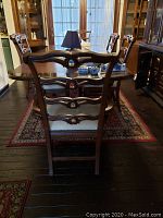 View of the six chairs arranged around a dining table, showcasing carved wooden backrests and textured seat cushions.