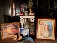 Wide shot showing full lot items including birdcage, shelves, framed prints, ceramic figurines, and decorative pieces on and around table.