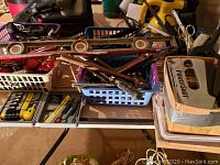 Photo showing bins with multiple hand tools including spirit levels, adjustable wrenches, hammers, screwdrivers, and clamps laid on a table