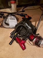 Photo showing cordless Worx Hydroshot power washer spray handle, battery pack, user manual, Monster vacuum storage bag, vacuum attachments, and a jar of wire ties