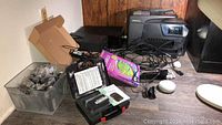 Overview of lot showing two printers, clear bin with small items, purple box, TENS unit case, power cords
