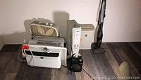 Wide view of five items: Utilitech oil-filled heater, Holmes air purifier, paper shredder, Bissell mini vacuum, and white Frigidaire air conditioner unit, all placed on a floor against a wall.