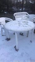 Top view of white plastic round patio table and five matching plastic chairs in outdoor snowy setting.
