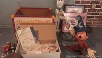 Wide view showing wooden Mickey Mouse toy box with contents, ceramic dolls, clowns and framed clown art in background