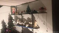 Shelf with ceramic Christmas tree, sleigh, reindeer, snow globe, and possibly white porcelain Santa figurine.