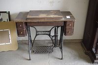 Front view of wooden cabinet with four small drawers and Singer treadle sewing machine base with foot pedal.