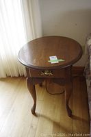 Front view of wood side table with drawer and cabriole legs showing scuffs on top.