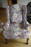 Full view of the fabric wingback chair showing floral upholstery and carved wooden legs.