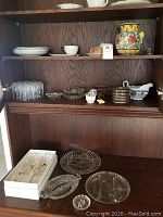 Wood shelf with white china plates, cups, gravy boat, and butter dish. Crystal glasses and bowls on middle shelf. Clear glass platters and bowls on lower section.