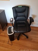 Black faux leather office chair with cushioned seat and backrest beside a black and silver Staples paper shredder on wooden floor.