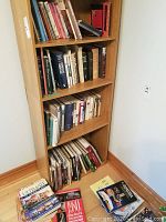 Bookshelf with multiple books of varied topics including local history and fiction, some books on floor spread out