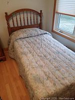Full view of twin bed with wood spindle headboard and floral quilted comforter, showing size and condition.