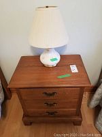 Solid wood side table with two drawers and brassy hardware, white ceramic lamp with pink floral design on top