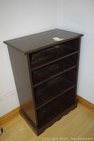 Front angled view of dark brown wooden bookcase showing four shelves and scalloped base, wood surface worn.
