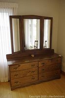 Front view of vintage solid pine dresser with attached tri-panel mirror and antique brush on top, showing six drawers and ornate metal handles.