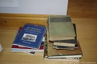 Stack of seven books including green hardcover and assorted softcovers on hardwood floor.