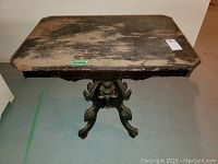 Top-front angle view of vintage wooden table showing rectangular top with heavy wear and scuffed surface and ornate pedestal base.